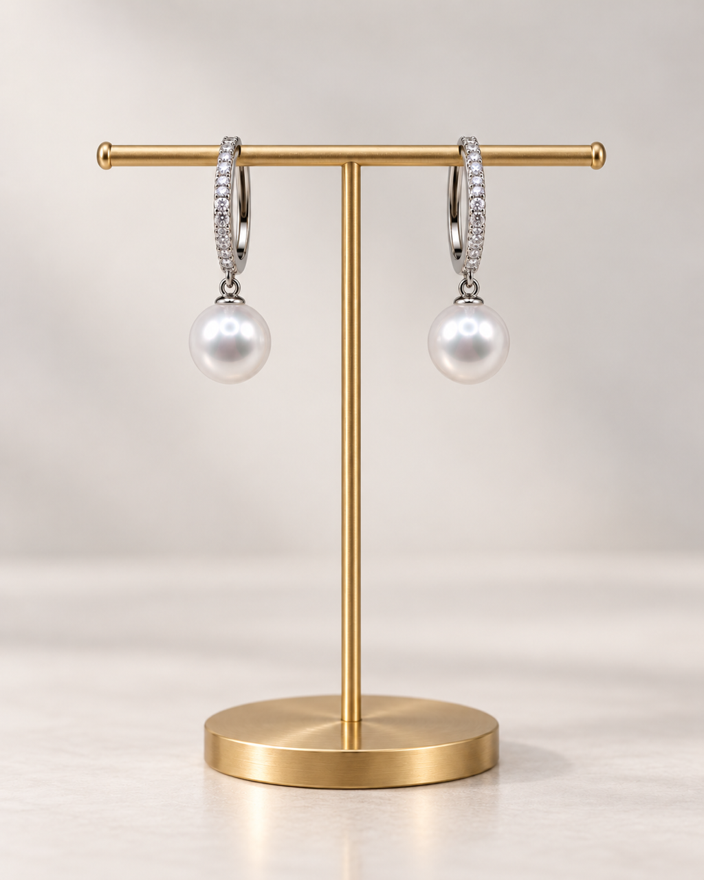 The 9mm White Freshwater Pearl Pavé Huggie Drop Earrings in sterling silver on a gold stand